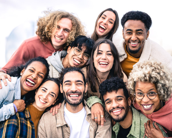 Multi ethnic guys and girls taking selfie outdoors with backlight - Happy life style friendship concept on young multicultural people having fun day together in Barcelona - Bright vivid filter.