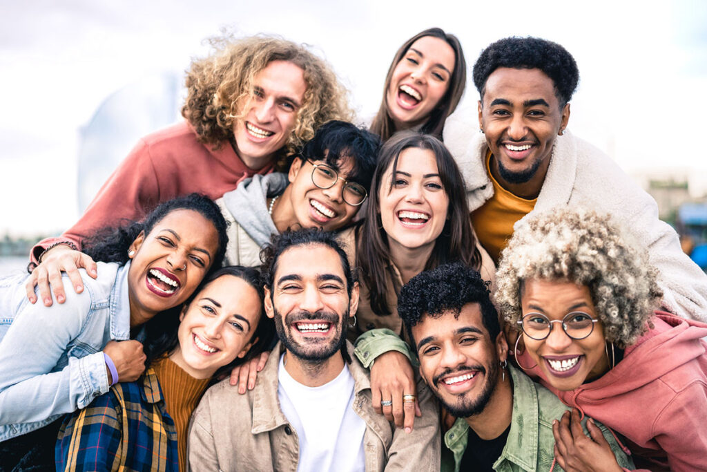 Multi ethnic guys and girls taking selfie outdoors with backlight - Happy life style friendship concept on young multicultural people having fun day together in Barcelona - Bright vivid filter.