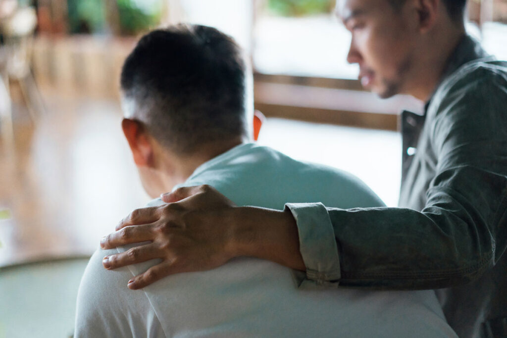 Rear view of a man comforting another man