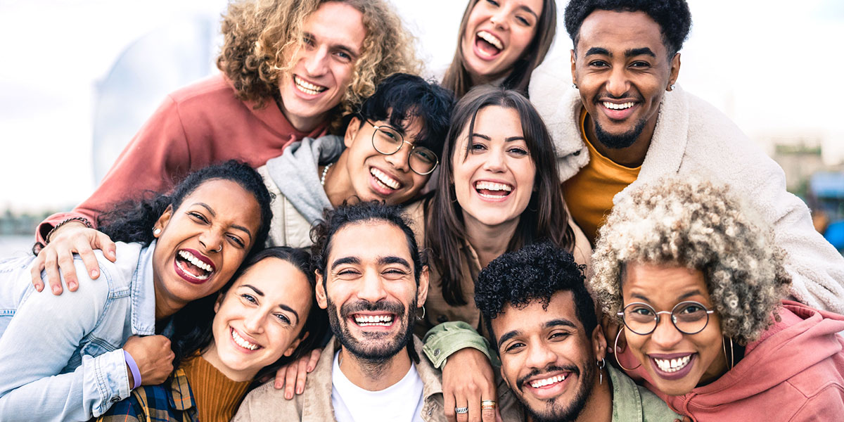 Multi ethnic guys and girls taking selfie outdoors with backlight - Happy life style friendship concept on young multicultural people having fun day together in Barcelona - Bright vivid filter.