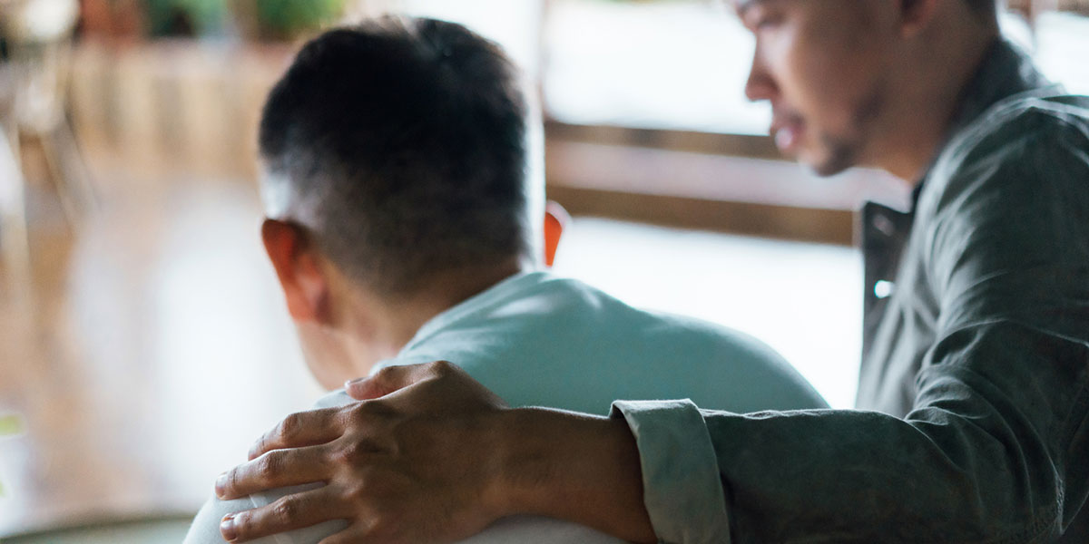 Rear view of a man comforting another man